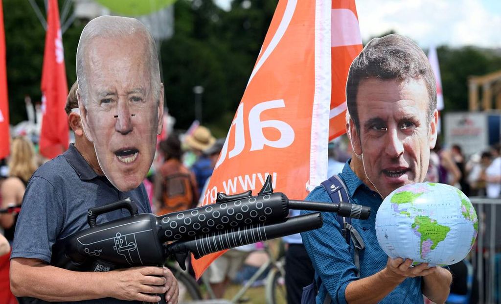 Pengunjuk rasa mengenakan topeng bergambar wajah Presiden AS Joe Biden dan Presiden Perancis Emmanuel Macron dalam demonstrasi yang digelar Greenpeace, Attac, dan organisasi-organisasi lain menjelang KTT G7 di Theresienwiese, Muenchen, Jerman selatan, 25 Juni 2022. 