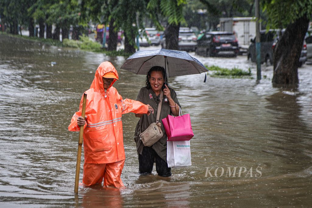 Petugas dari Dinas Lingkungan Hidup DKI Jakarta membantu warga yang menerobos genangan air di kawasan Cempaka Putih, Jakarta Pusat, Kamis (29/2/2024). 