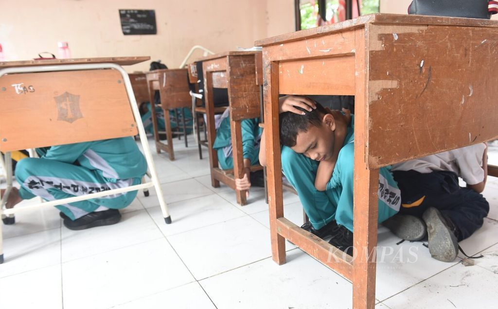 Siswa menyelamatkan diri di bawah meja saat simulasi penanganan bencana gempa bumi di SMPN 27 Surabaya, Kota Surabaya, Jawa Timur, Selasa (29/11/2022). Kegiatan tersebut diselenggarakan Badan Penanggulangan Bencana Daerah dan Dinas Pendidikan Kota Surabaya.
