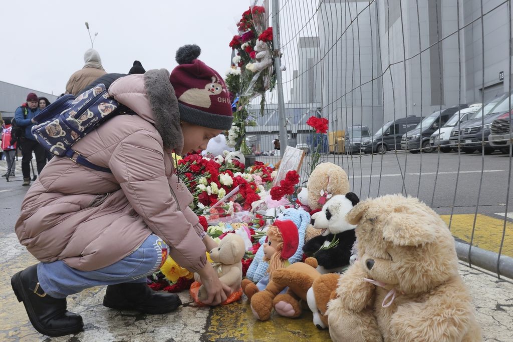 Seorang anak meletakkan mainan di pagar sebelah Balai Kota Crocus, di Moskwa, Rusia, pada 23 Maret 2024, menyusul serangan yang diklaim oleh kelompok NIIS.