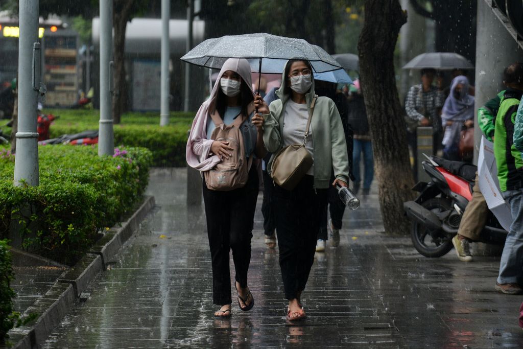 Dua perempuan berbagi payung saat hujan di Jalan Jenderal Sudirman, Jakarta Pusat, Jumat (5/5/2023). Jakarta kembali diguyur hujan pada Jumat sore bertepatan dengan jam pulang kantor.