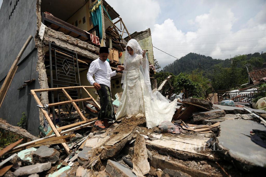 Muhammad Nurdin berjalan bersama istrinya, Nida Khovia Syukur, di depan rumah kerabat yang tadinya akan menjadi lokasi resepsi pernikahan yang hancur akibat gempa di Desa Mangunkerta, Kecamatan Cugenang, Kabupaten Cianjur, Jawa Barat, Minggu (4/12/2022). 