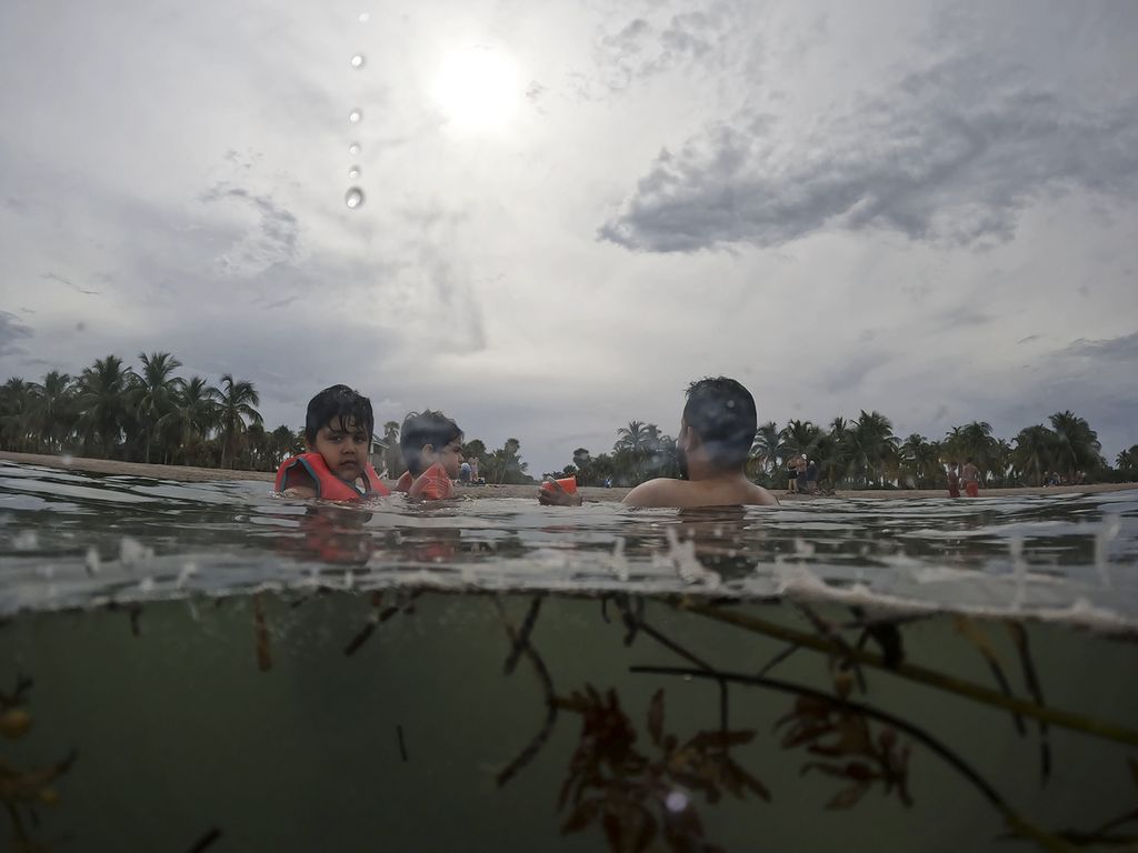 Galo Felipe Espinoza Sanchez (kiri) berendam bersama dengan ayah dan sepupunya di pantai Crandon Park, Key Biscayne, Florida pada 28 Juli 2023. Pemanasan global telah menyebabkan Juli menjadi bulan terpanas.