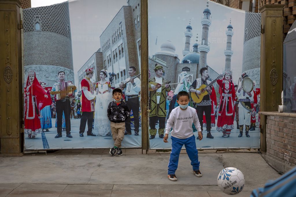 Sejumlah anak bermain sepak bola di depan sebuah gerbang dengan mural musisi Uighur di International Grand Bazaar, Urumqi, Xinjiang, China, 21 April 2021. 