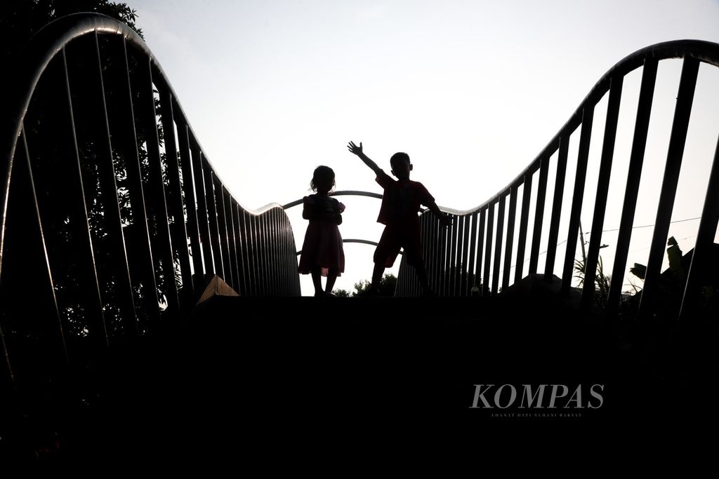 Siluet dua anak ketika bermain di jembatan di atas Kali Ciliwung, Kecamatan Pademangan, Jakarta Utara, Kamis (3/8/2023). 