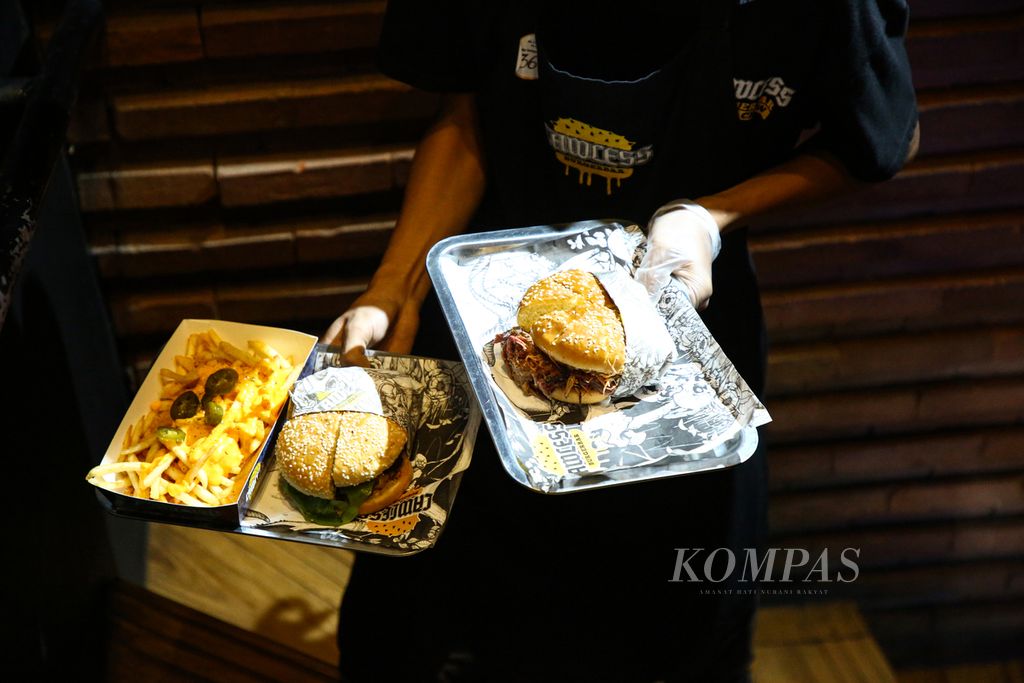 Pramusaji mengantarkan burger pesanan pengunjung di Lawless Burgerbar di kawasan Kemang, Jakarta Selatan, Selasa (1/6/2021).