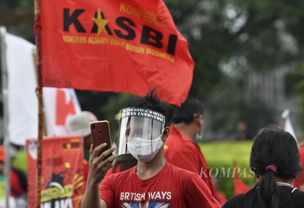 Salah seorang buruh melakukan panggilan layanan telepon video mengikuti aksi menentang pengesahan RUU Cipta Kerja oleh DPR, di kawasan Tugu Tani, Jakarta Pusat, Selasa (20/10/2020). 