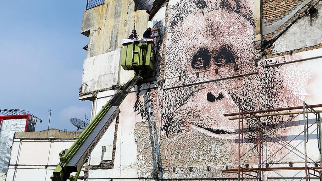 Pegiat seni mural asal Portugal, Alexandre Farto (di atas tangga), membuat mural wajah orangutan sumatera di sebuah dinding rumah toko di dekat Tugu Air Mancur, Medan, Sumatera Utara, Sabtu (24/3/2018). Orangutan dan spesies lainnya terancam punah akibat perambahan hutan yang masif.