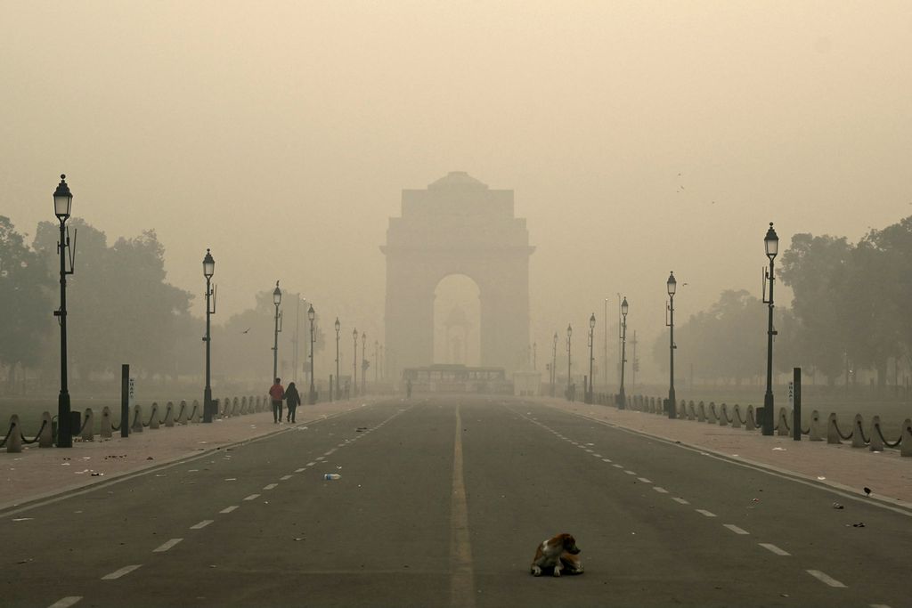 Pejalan kaki melintas di tengah buruknya kabut polusi udara di New Delhi, Senin (13/11/2023).