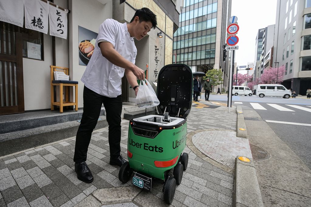 A restaurant employee ordered food from an unmanned robot during a trial of robot delivery service by Uber Eats Japan, Mitsubishi Electric, and robot developer Cartken in downtown Tokyo, Japan on Tuesday (5/3/2024).