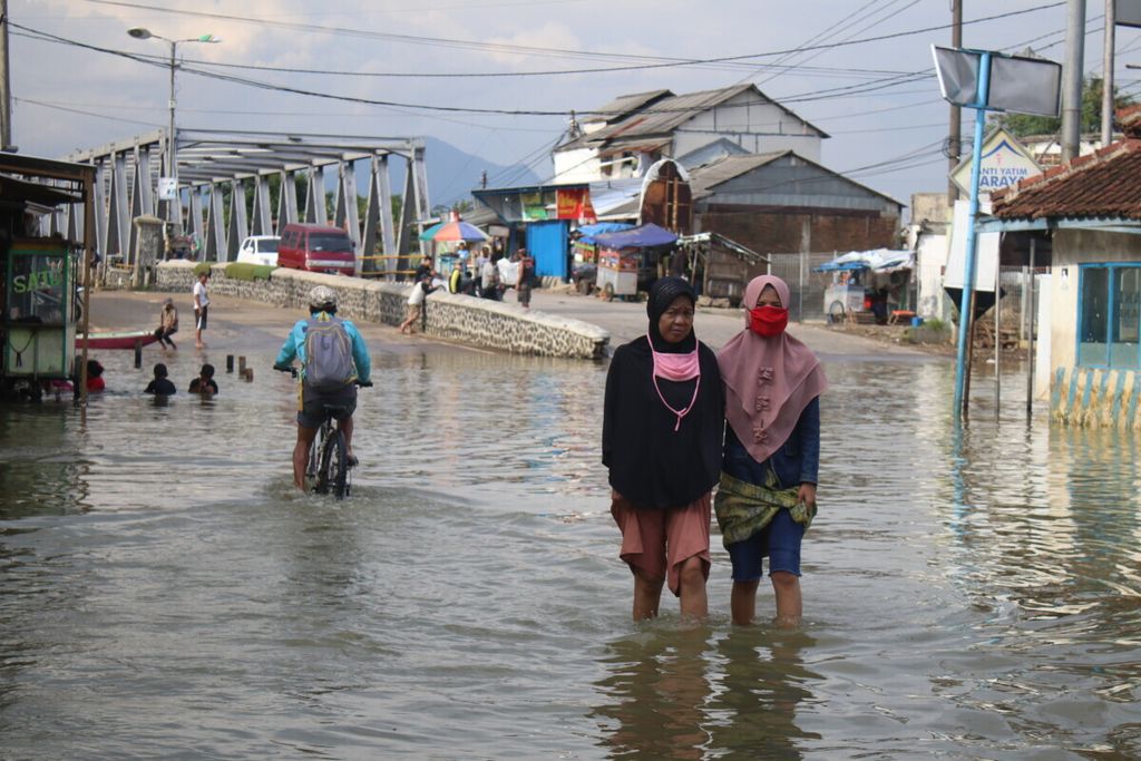 Residents crossing Jalan Raya Banjaran which was submerged by river water, Saturday (2/5/2020)
