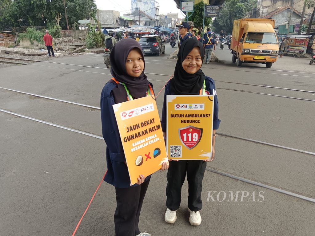 Dua anggota muda Komunitas Edan Sepur Bandung, Jihaan Syifaa Syauqi (17) dan Zunimar Nurul Hidayah (16),  saat menyosialisasikan keselamatan berkendara di pelintasan kereta api dekat Stasiun Kiaracondong, Kota Bandung, Jawa Barat, Jumat (22/3/2024).