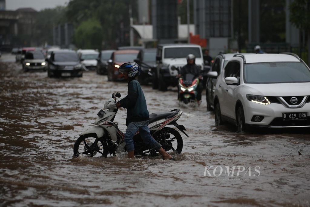 Residents push their stalled motorcycles as they try to pass through flooded Boulevard Raya Road in Kelapa Gading, Jakarta, on Thursday (29/2/2024).
