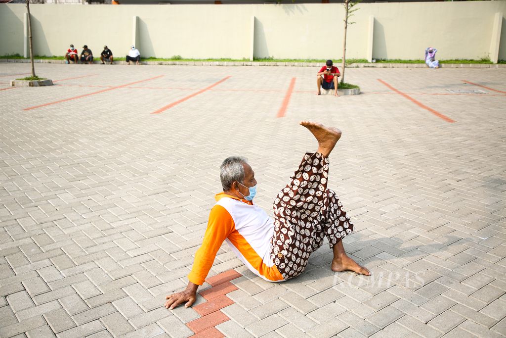 Seorang warga lanjut usia menggerakkan kakinya sambil berjemur di area parkir gedung pertemuan di kawasan Larangan, Kota Tangerang, Banten, Juli 2021.
