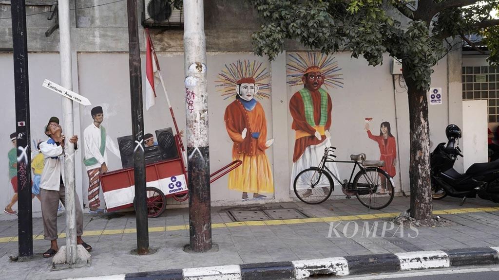 Pengojek sepeda menunggu penumpang di depan mural kampung tematik sketsa di Penjaringan, Jakarta Utara, Kamis (14/2/2019). Pengecatan mural bernuansa ”Jakarta Tempo Doeloe” tersebut menarik perhatian wisatawan yang berjalan-jalan di kawasan Kota Tua.