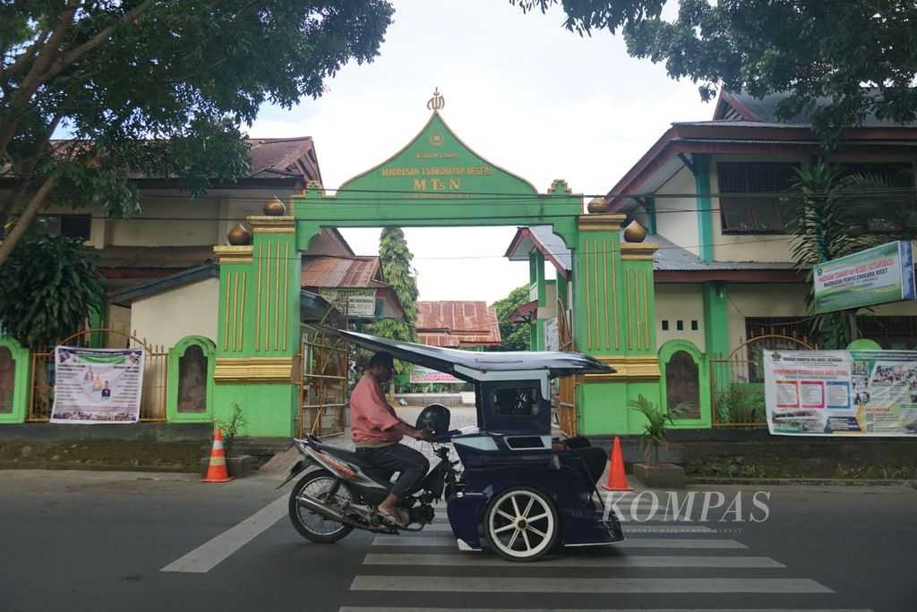 Pengemudi bentor atau bendi motor melintas di depan gerbang Madrasah Tsanawiyah Negeri 1 Kotamobagu, Gogagoman, Kotamobagu, Sulawesi Utara, Rabu (15/6/2022). Seorang siswa meninggal setelah mengaku menjadi korban penganiayaan di dalam area sekolah.