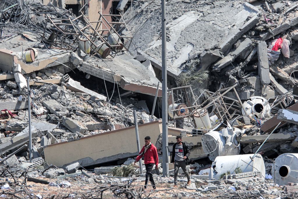 Palestinian residents walk amidst the ruins of buildings that have been destroyed in the Asra residential complex, northwest of Nuseirat in the Gaza Strip, on Monday (25/3/2024) local time.