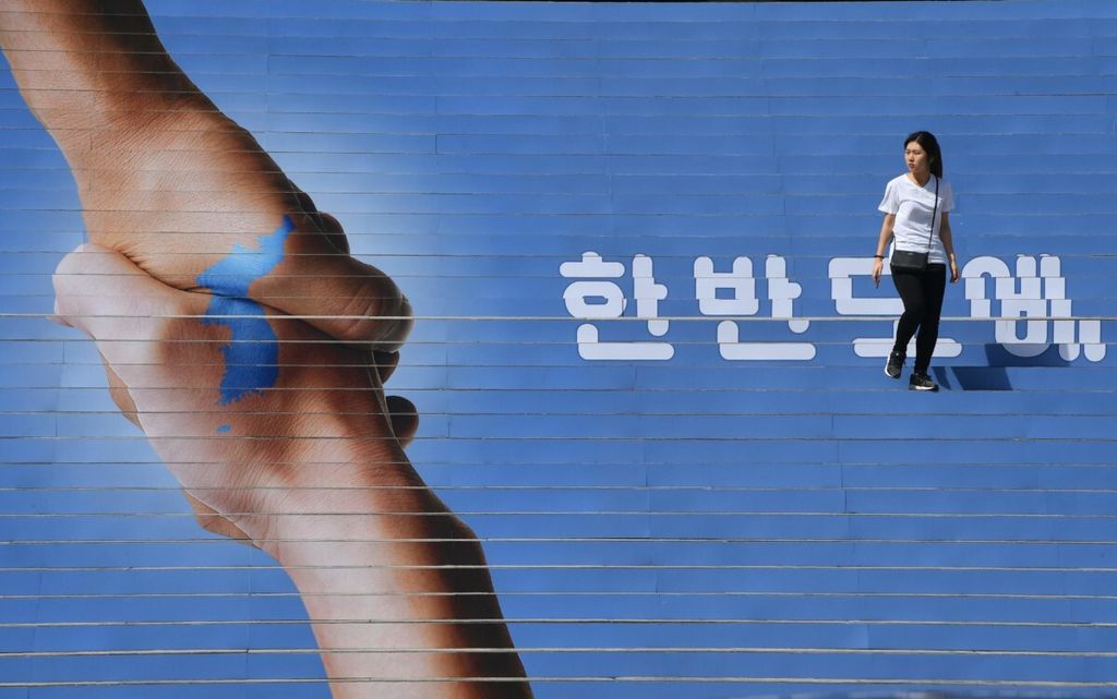 Seorang warga berjalan di tangga yang ditempeli gambar dua tangan yang saling menggenggam dan membentuk Semenanjung Korea untuk mendukung pertemuan Presiden Korea Selatan Moon Jae-in dan Pemimpin Korea Utara Kim Jong Un. Gambar ini dipasang di Seoul, Korsel, Senin (17/9/2018).