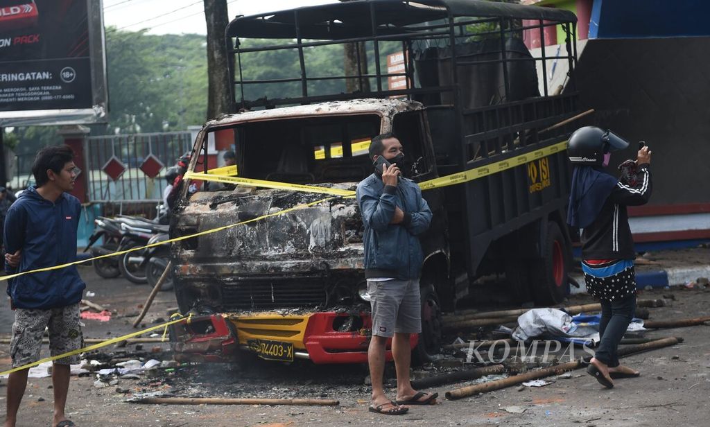 Warga berada di dekat bangkai truk polisi yang rusak terbakar saat kerusuhan sehari sebelumnya di Stadion Kanjuruhan, Kabupaten Malang, Jawa Timur, Minggu (2/10/2022). 