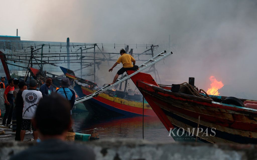 Salah satu warga berusaha meraih selang untuk memadamkan api yang membakar kapal nelayan di Pelabuhan Perikanan Pantai Tegalsari, Kota Tegal, Jawa Tengah, Selasa (15/8/2023). 