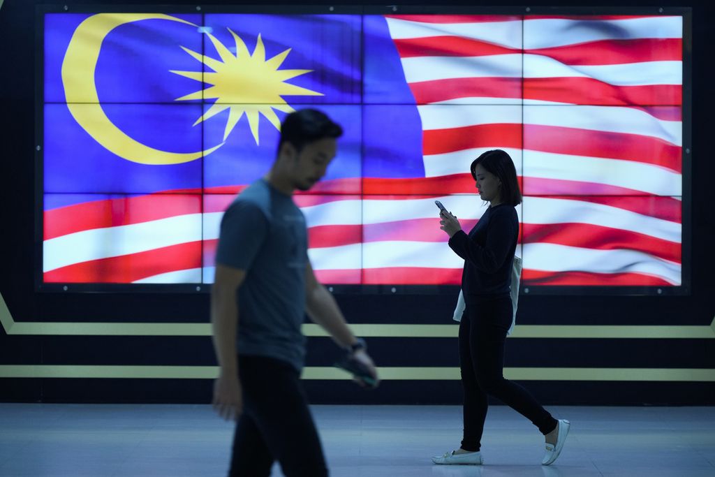 Pejalan kaki melintas di depan layar pengumuman pemilu, yang menayangkan bendera Malaysia, di Kuala Lumpur, Malaysia, 21 November 2022. 