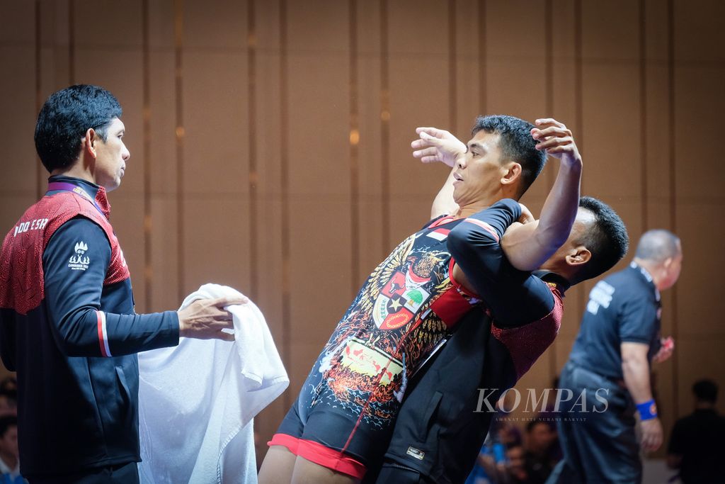Pegulat Indonesia, Muhammad Aliansyah (tengah), saat istirahat dalam pertandingan SEA Games Kamboja 2023 di Chroy Changvar International Convention and Exhibition Center, Phnom Penh, Kamboja, Minggu (14/5/2023). Aliansyah ditangani langsung oleh sang kakak, Rudiansyah (di balik tubuh Aliansyah), yang merupakan pelatih tim gulat Indonesia.