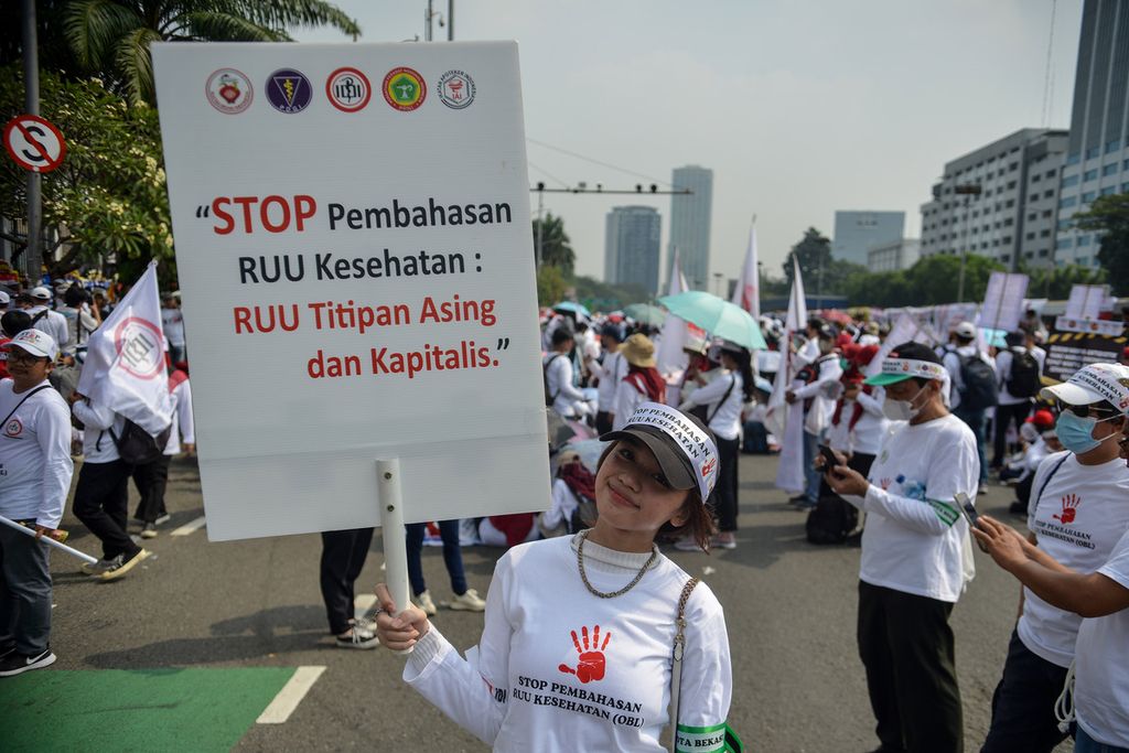 Seorang tenaga kesehatan membawa poster berisi tuntutan untuk menghentikan pembahasan Rancangan Undang-Undang (RUU) Kesehatan di depan gedung DPR, Jakarta Pusat, Senin (5/6/2023). 