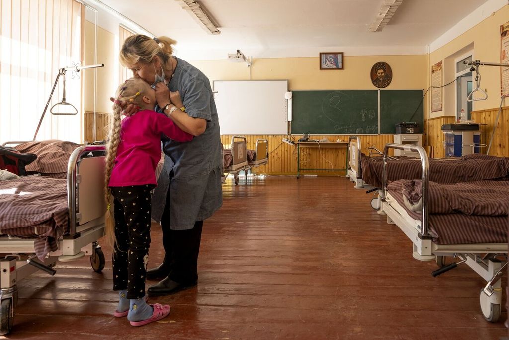 Nadia mencium cucu perempuannya yang berusia 10 tahun, Zlata Moiseinko, yang menderita penyakit jantung saat dia menjalani perawatan di gedung sekolah yang telah diubah menjadi rumah sakit darurat di Mostyska, Ukraina, Kamis (24/3/2022). 
