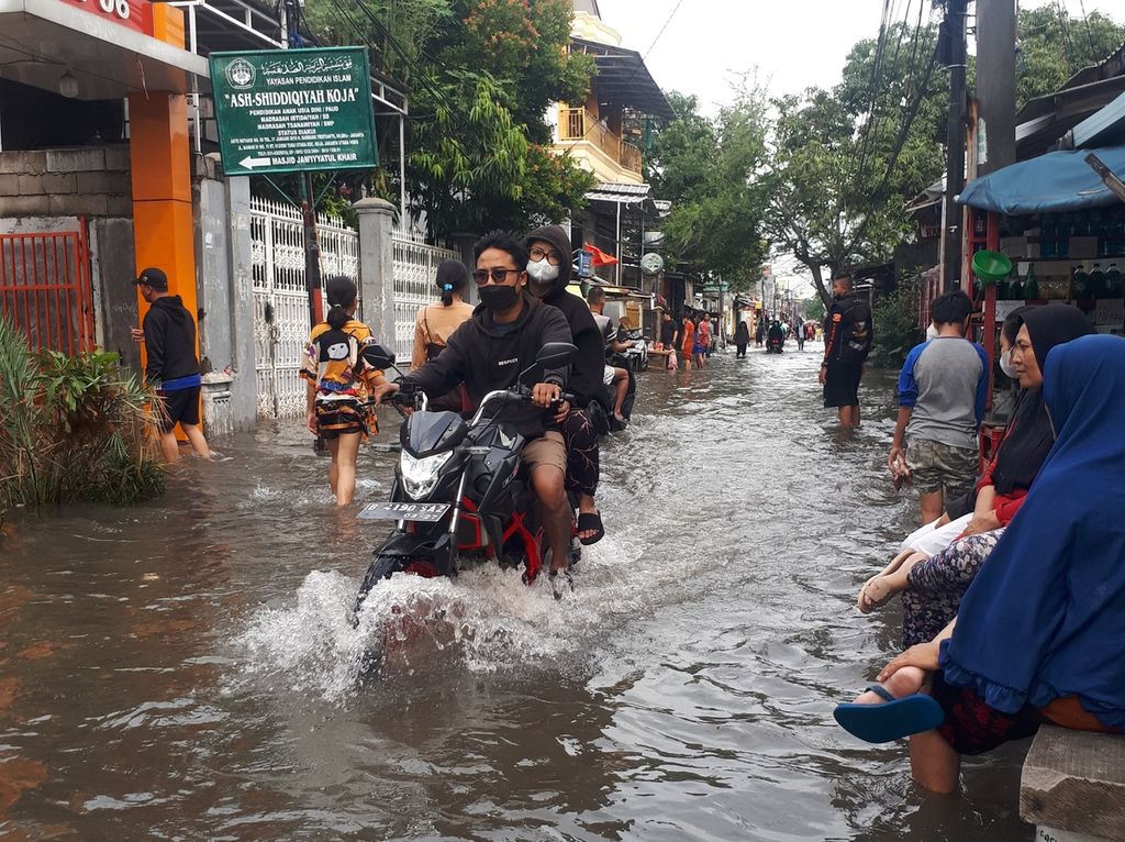 Warga melewati genangan air menggunakan sepeda motor di Jalan Manggar, Tugu Utara, Koja, Jakarta Utara, Minggu (1/1/2023).