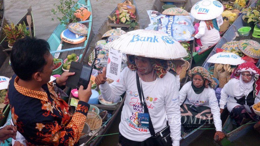 Pengunjung melakukan pembayaran digital menggunakan <i>Quick Response Code Indonesian Standard</i> (QRIS) saat berbelanja di pasar terapung dalam kampanye Gerakan Nasional Bangga Buatan Indonesia di Banjarmasin, Kalimantan Selatan, Jumat (22/7/2022). 