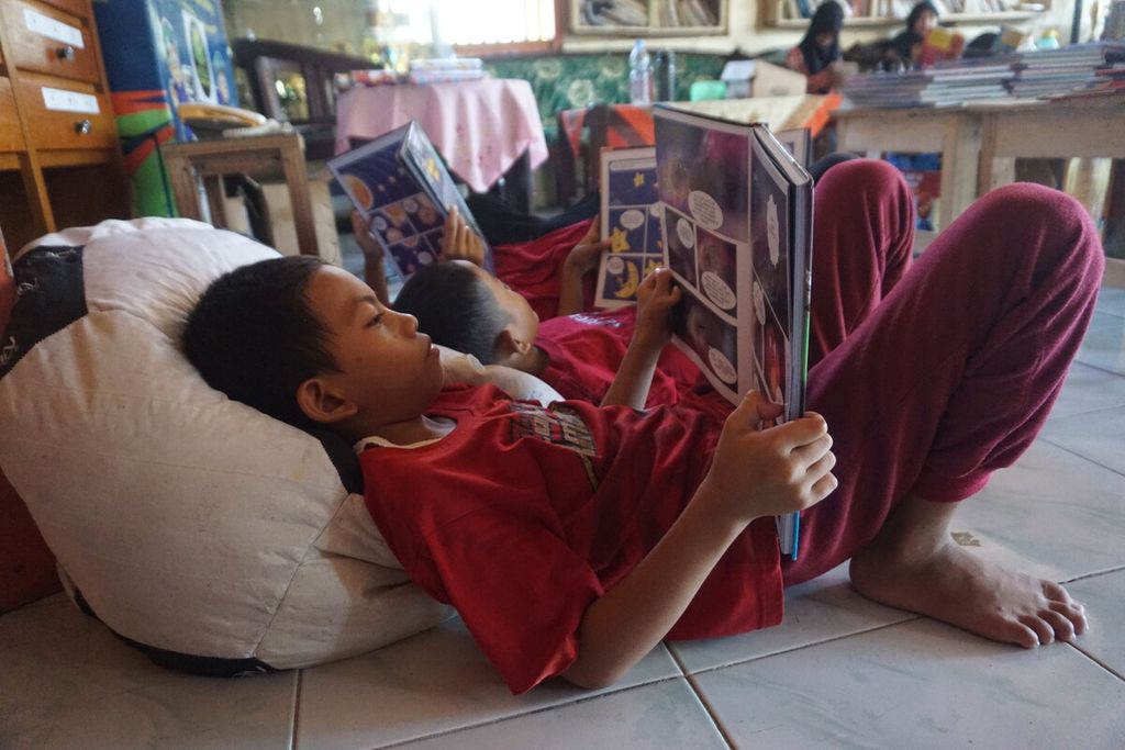 Arjun Dwi Antoro (8) dan teman-temannya rebahan membaca buku di kursi santai di Perpustakaan Bergerak Limbah Pustaka di Desa Muntang, Kecamatan Kemangkon, Kabupaten Purbalingga, Jawa Tengah, Minggu (30/4/2023).