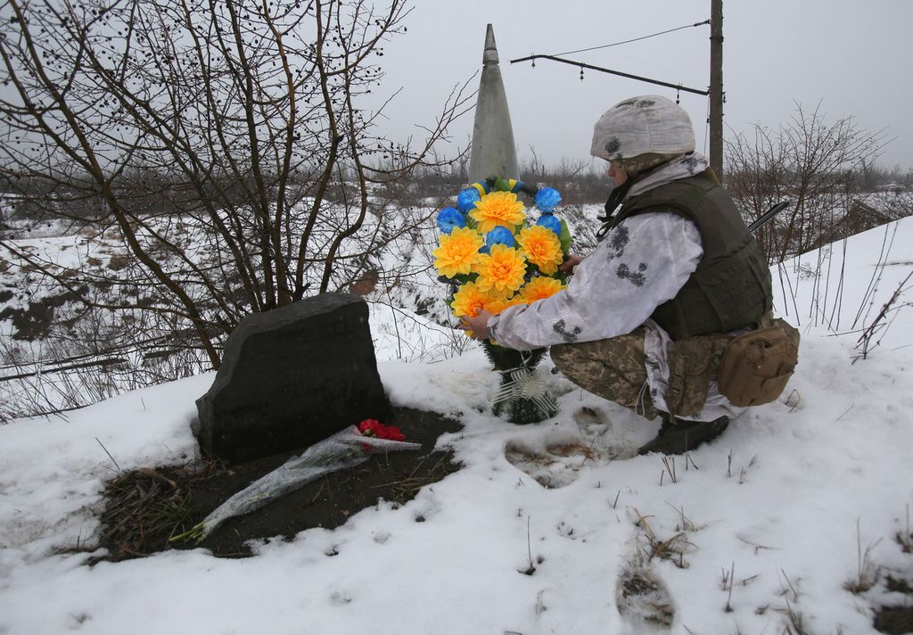 Seorang prajurit Ukraina, 2 Februari 2022, meletakkan bunga dengan warna senada dengan bendera negaranya ke tempat salah satu rekannya terbunuh pada 2017 di garis depan pertempuran melawan kelompok separatis dukungan Rusia di dekat Avdiivka, Donetsk, Ukraina.  