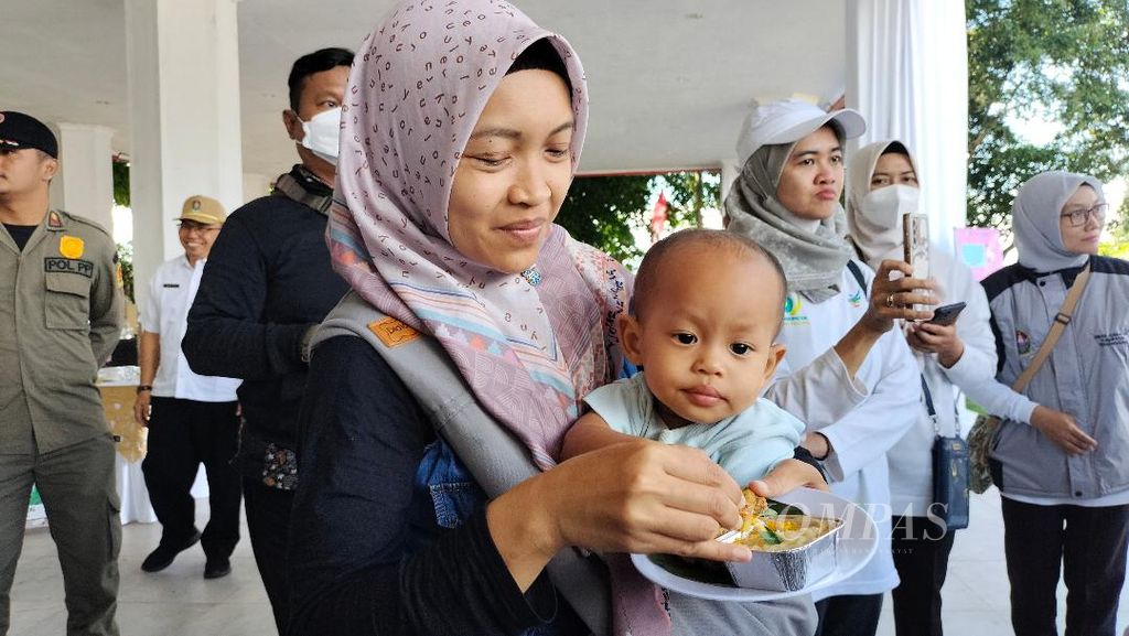 Dalam gendongan ibunya, seorang bayi menyantap makanan tambahan yang disediakan oleh Pemerintah Kabupaten Temanggung dalam acara <i>kick off</i> gerakan bersama mengatasi tengkes di Alun-alun Temanggung, Jumat (12/5/2023).