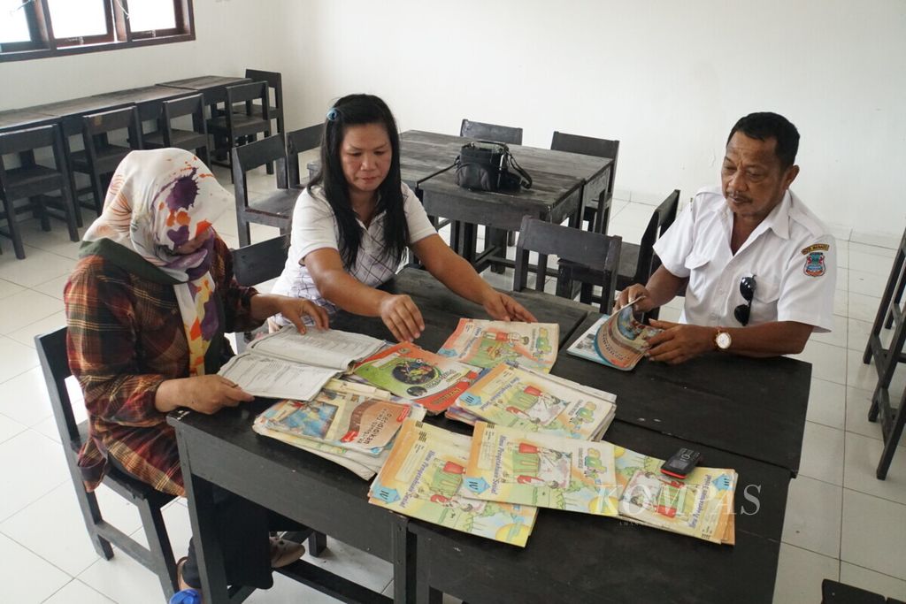 Guru SD Negeri Pandu Cerdas, Aguste Bangsuil (55, kanan), bersama dua warga permukiman relokasi korban banjir Manado, Maria Tangel (44) dan Siti Aisyah Yusuf (33), merapikan buku bahan ajar di SDN Pandu Cerdas, Manado, Sulawesi Utara, Rabu (24/7/2019).