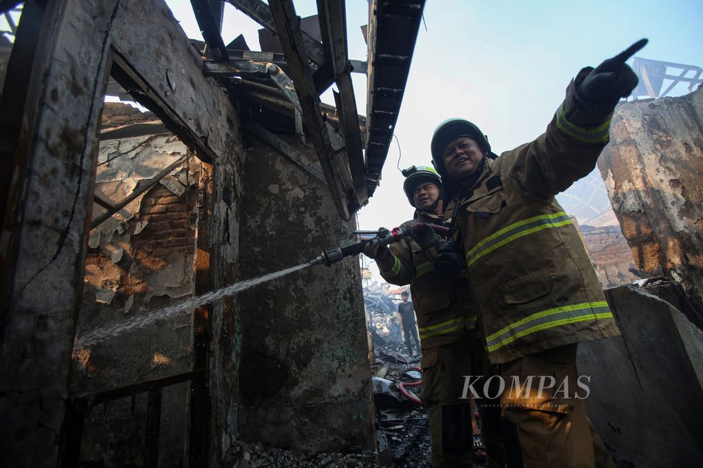 Dua petugas pemadam kebakaran mendinginkan salah satu rumah yang terbakar di Kampung Bali Matraman, Manggarai, Jakarta Selatan, Selasa (13/8/2024). 