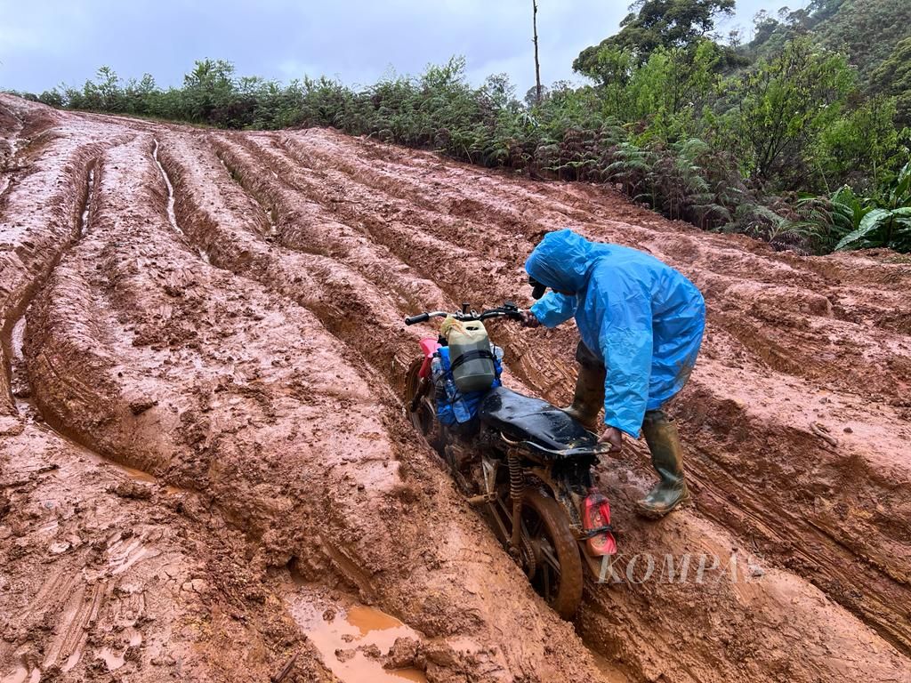 Seorang pengojek mengangkat kendaraan roda dua yang terbenam dalam lumpur dalam perjalanan ke Seko, Luwu Utara, Sulawesi Selatan, Senin (4/7/2022).