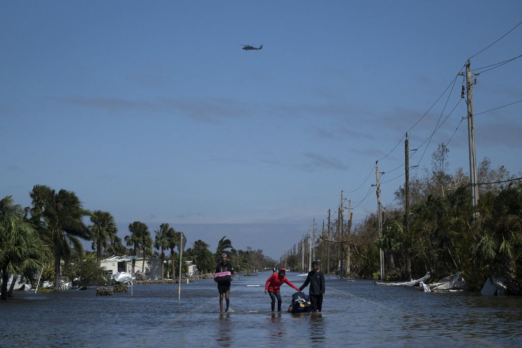 Orang-orang membawa barang-barang mereka menembus banjir setelah badai Ian melanda Fort Myers, Florida, Kamis (29/9/2022).