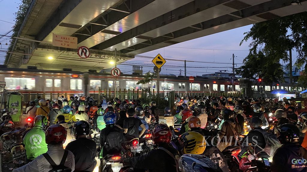 Pengguna sepeda motor menunggu kereta api melintas di pelintasan sebidang di kawasan Gambir, Jakarta Pusat, Jumat (19/5/2023). Pelintasan sebidang yang ditutup tiang besi tersebut menyisakan ruang 2 meter yang digunakan untuk lalu lalang warga.  