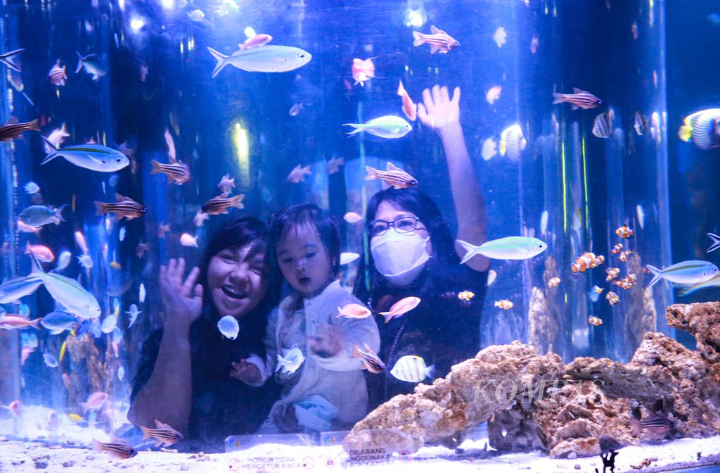 Pengunjung berpose untuk difoto dari balik akuarium di Jakarta Aquarium Safari di Jakarta, Jumat (15/4/2022).