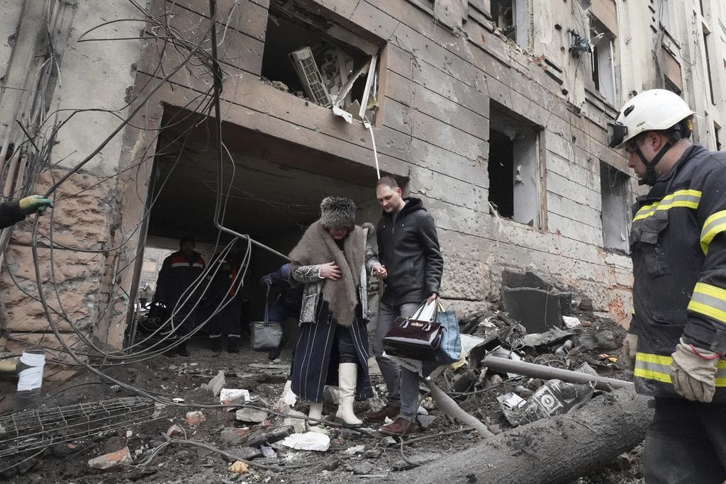 Seorang pria membantu seorang perempuan berjalan keluar dari gedung apartemen yang dihantam roket Rusia di pusat kota Kharkiv, Ukraina, Minggu (5/2/2023). 