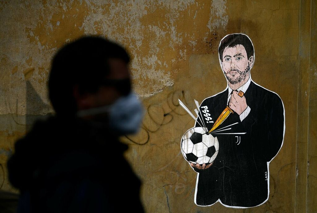Seorang pria berjalan melewati tembok di dekat kantor Federasi Sepak Bola Italia di Roma, 21 April 2021. Seniman Italia, Laika, melukis sosok Presiden Juventus Andrea Agnelli sedang menggemboskan bola dengan pisau.