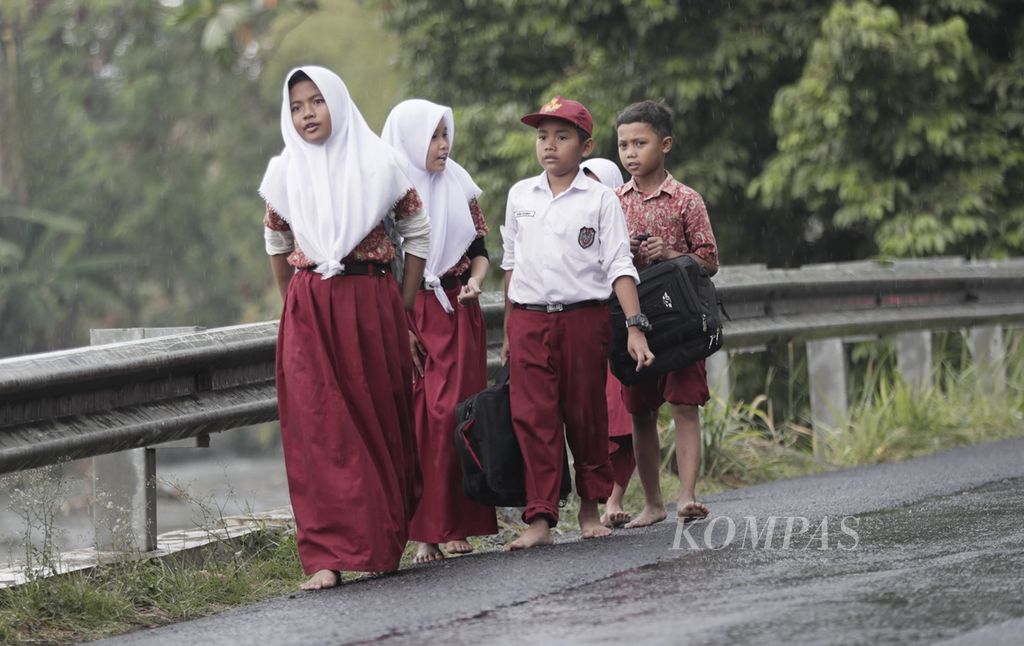 Para siswa sekolah dasar pulang sekolah dengan bertelanjang kaki saat hujan mulai mengguyur kawasan Katulampa, Bogor, Jawa Barat, Kamis (22/8/2019). 