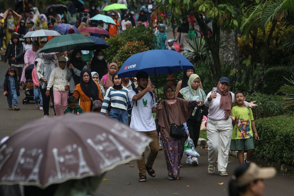 Sejumlah pengunjung menggunakan payung saat hujan di Kebun Binatang Ragunan, Jakarta Selatan, Rabu (28/12/2022). Warga tetap antusias berwisata di tengah potensi cuaca ekstrem.