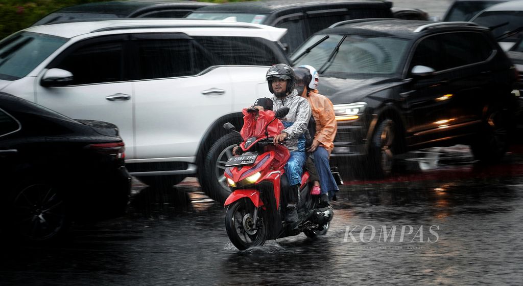Warga dan keluarganya berboncengan menggunakan sepeda motor dan melintasi kawasan Bundaran Hotel Indonesia, Jakarta, saat hujan lebat mengguyur, Minggu (31/3/2024).  
