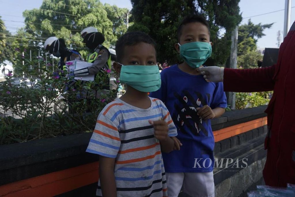 Anak-anak berjalan-jalan di kawasan Alun-alun Magelang, Jawa Tengah, sembari mengenakan masker, April lalu. Kelompok usia anak-anak adalah kelompok yang sangat rentan tertular Covid-19.