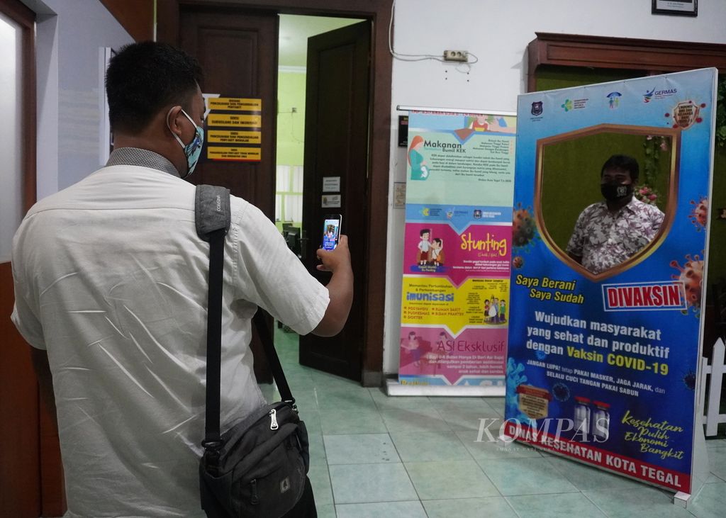 Warga berfoto seusai disuntik vaksin Covid-19 di Dinas Kesehatan Kota Tegal, Jawa Tengah, Jumat (16/4/2021) malam. Selama Ramadhan, Dinas Kesehatan Kota Tegal melayani vaksinasi malam hari mulai pukul 19.00-21.00. Layanan ini diberikan kepada warga yang tidak bisa mengikuti vaksinasi pada siang hari.