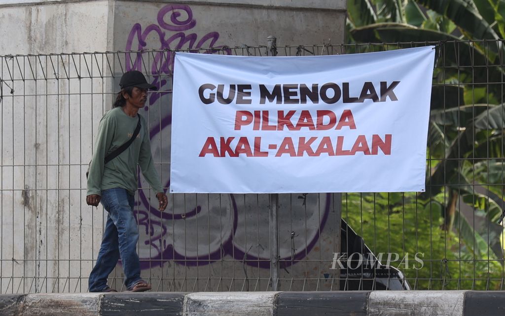 Warga melintas di dekat tulisan terkait Pilkada Jakarta di kawasan Pondok Kelapa, Jakarta, Selasa (20/8/2024). 