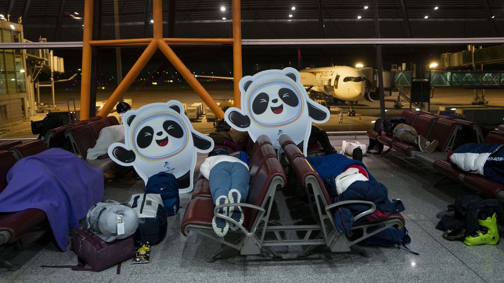 Calon penumpang tidur di kursi di sebelah maskot Olimpiade Bing Dwen Dwen di Bandara Internasional Ibu Kota Beijing, China, setelah Olimpiade Musim Dingin 2022, Senin (21/2/2022). 