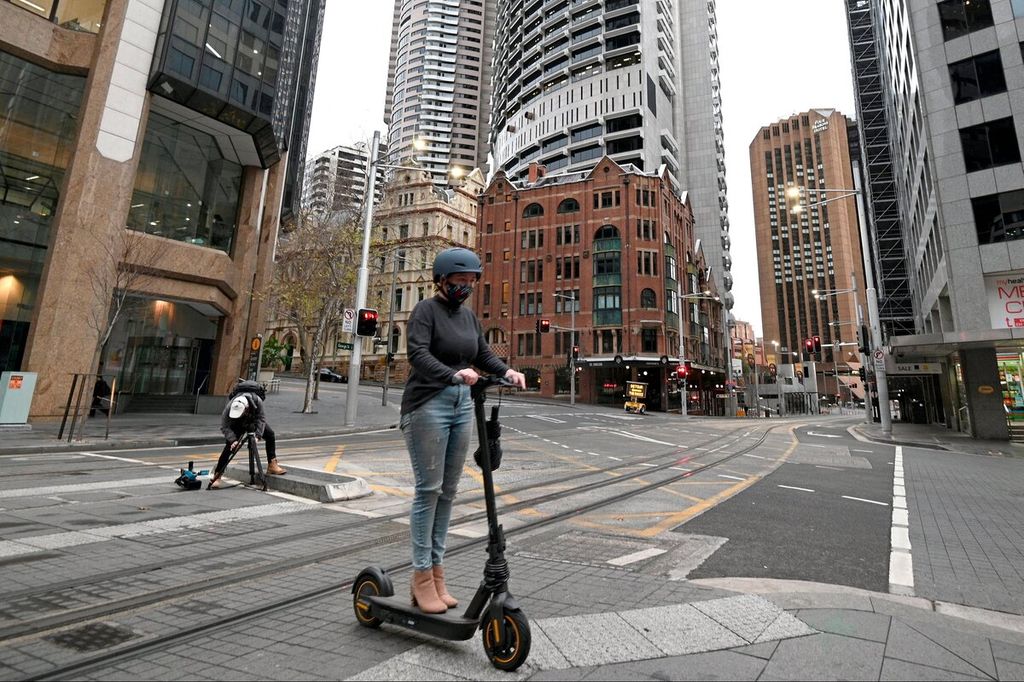 Seorang gadis mengendarai skuter listriknya melalui kawasan pusat bisnis yang lengang saat diberlakukan karantina wilayah di Sydney, Australia, Jumat (23/7/2021). 