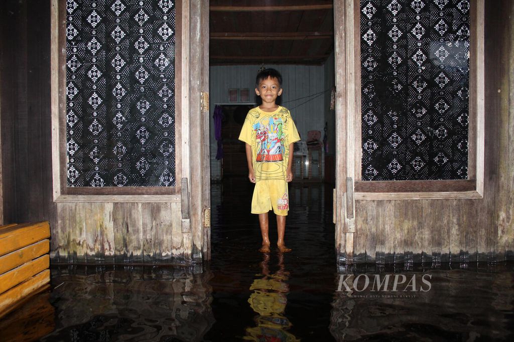 Seorang anak menunggu banjir surut di rumahnya di Desa Dusun Jutuh, Kabupaten Barito Selatan, Kalimantan Tengah, Rabu (24/1/2024). Banjir mencapai 1 meter lebih di jalur Trans-Kalimantan dari Kalteng menuju Kalimantan Timur. Trans-Kalimantan pun putus.